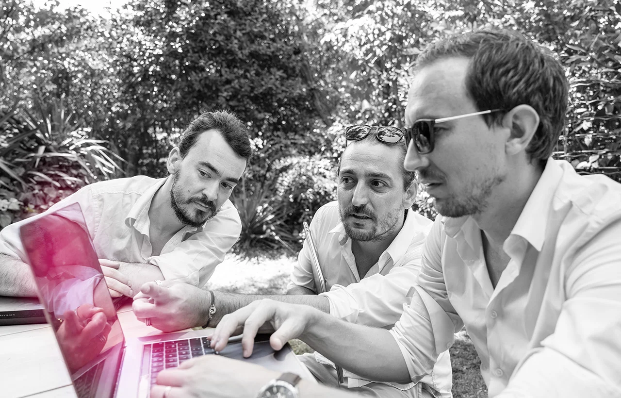 Conseils et techniques SEO pour mieux référencer votre site 1 Trois adultes réunis autour d’un ordinateur portable dans un environnement extérieur végétalisé.